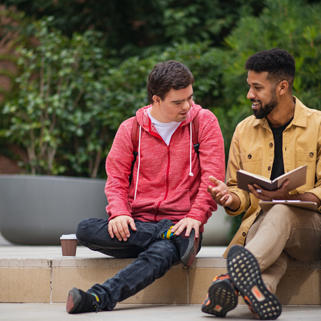 A young man with Down syndrome and friend sitting and talking outdoors.