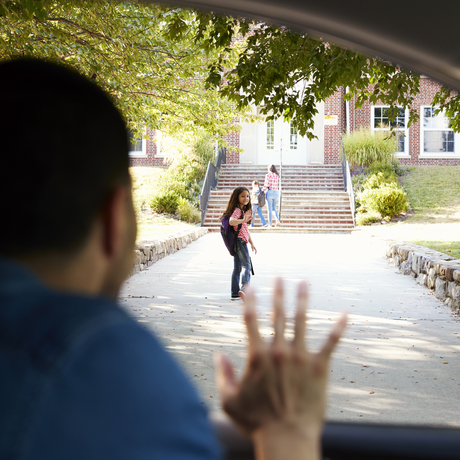 Un père assis dans une voiture dépose sa fille à la porte d’une école.