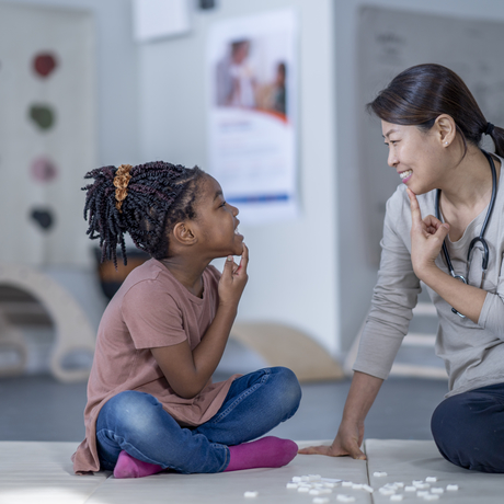 A therapist sits beside her young patient as they work on speech therapy exercises.