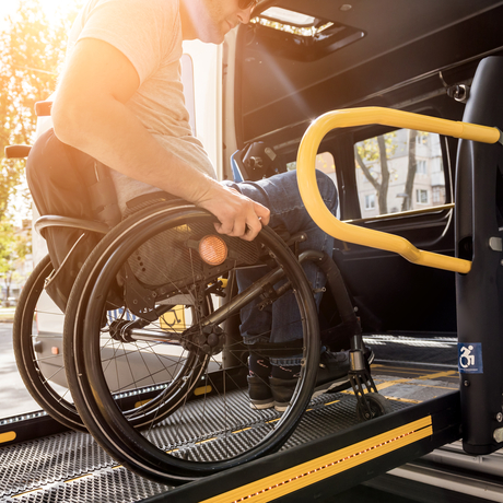 A man in a wheelchair on a lift of a vehicle for people with disabilities.